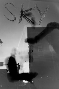 a black and white photo of a person in a window with the word sky written on it